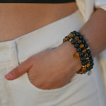 hand in a jean pocket showing off the three piece brave bracelet with tiger's eye, black onyx, and gold I am brave charm